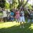 Pixelated outdoor scene with multiple figures in colorful clothing standing on grass under trees.