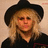 Pixelated image of a person with blonde hair wearing a black hat and dark clothing against a light background.