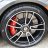 A circular metallic wheel with a red brake caliper visible through the spokes, set against a blurred background.