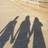 Three dark silhouetted figures stand against a light beige background with subtle horizontal gradient.