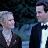 Pixelated static image of two stylized human figures in formal attire against a dark background with blue-green gradient elements.