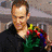 A man in a black shirt holds a colorful bouquet while another man in a white shirt gestures with open hands against a blurred background.