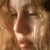 A pixelated close-up of a person's face with light brown hair, showing eyes, nose, and mouth in warm tones.