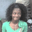 Pixelated static image of a person with voluminous dark curly hair wearing a light green top against a blurred background.