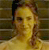 Pixelated static image of a person with light brown hair tied back, wearing a light-colored top against a blurred background.