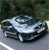 Pixelated image of a silver sedan on a gray road with a blurred green background, appearing as a low-resolution digital icon.