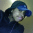 Pixelated static image of a person wearing dark blue clothing and a blue cap, with light-colored background.