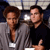 Two people stand side-by-side in a pixelated image; the person on the left wears a gray jacket with a white name tag, while the person on the right wears a dark shirt and gives a thumbs-up gesture.