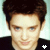 A pixelated close-up of a person with dark hair and light skin wearing a black top, showing two sequential facial expressions.