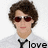 Pixelated image of a person with brown curly hair, red-tinted sunglasses, light skin tone, and pink lips wearing a white shirt and black tie against plain background.