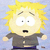 Pixelated cartoon character with spiky yellow hair, wide eyes, and open mouth wearing dark gray shirt against light blue background.