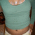 A person wearing a teal long-sleeve crop top and light-colored shorts, with visible navel and hand near hip.