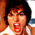 Pixelated static image of a person with dark hair and an open mouth, wearing a white sleeveless top against a brown background.