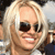 A pixelated close-up of a person with light-colored hair wearing dark sunglasses and a white top, smiling with visible teeth.