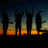 Silhouettes of four figures with raised arms against a sunset sky transitioning from dark blue to orange and yellow.