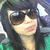 A person with long dark hair and sunglasses wears a green top, shown in three slightly varied poses against a blurred background.