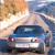 Pixelated static image of a blue car viewed from the rear, positioned on a road with blurred background elements suggesting motion or speed.