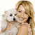 A woman with long blonde hair holds a small white dog against a plain background, smiling broadly in three