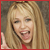 Pixelated close-up of a smiling person with long blonde hair wearing red clothing and making a peace sign gesture.