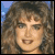 Pixelated static image of a person with long curly brown hair against a blue background, rendered in low-resolution 256x256 pixels with visible dithering and color blending.