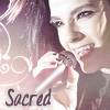 A close-up of a person holding a microphone with a pinkish-purple gradient background and decorative swirls, with the word 'Sacred' in dark brown text at the bottom left.