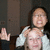 A person in a white jacket holds another person's head with both hands, making an exaggerated facial expression while raising one hand.