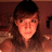 Pixelated static image of a person with long brown hair and a dark cap, wearing a light-colored top against a warm-toned background.