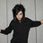 Pixelated figure in black hoodie with arms extended against gray vertical panel background.