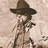 Pixelated figure wearing a wide-brimmed brown hat and light-colored trench coat, holding a dark object near the chest against a beige background.