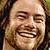 Pixelated close-up of a person with light skin tone, dark brown hair, and a broad smile showing teeth, set against a blurred background.