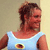 Pixelated image of a person with dark hair tied up, wearing a light blue sleeveless top with a circular design on the chest, against a plain background.