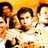 Pixelated group of people in white shirts against orange background with blue text at bottom.