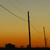 Pixelated sunset scene with three vertical structures against orange and yellow gradient sky, dark silhouette at base.