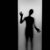 Pixelated grayscale silhouette of a humanoid figure holding a long object in one hand, standing against a gradient background with a vertical black border on the left.