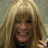 Pixelated static image of a person with long blonde hair and bangs, wearing a dark top against a muted background.