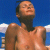 Pixelated image of a person with short dark hair, bare shoulders, and a black neckband against a blue sky with white clouds.