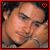Pixelated portrait of a person with dark hair and light skin, wearing a striped shirt, framed by red border with heart symbol.