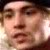 Pixelated close-up of a person's face with visible eyes, nose, and mouth, rendered in warm brown and beige tones against a dark background.
