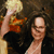 Two figures in a pixelated image: one with light hair holding a golden object, the other with dark hair and glasses, both in dark clothing against a dark background.
