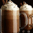 Two pixelated mugs of dark brown liquid topped with white foam, side-by-side against a black background.