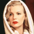 Pixelated close-up of a person with light brown hair, red lips, and a white garment against a dark background.