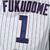 A white pinstriped baseball jersey with dark blue text and number, showing repeated 'FUKUOME' above a large '1'.