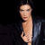 Static pixelated image of a person with dark hair wearing a black jacket over a light-colored shirt against a solid black background.