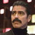 Pixelated close-up of a person with dark hair, mustache, and dark clothing against a dark background with scattered light-colored shapes.