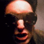 20 identical frames showing a person wearing dark sunglasses and a dark jacket against a dark background, with subtle variations in facial expression and lighting