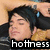 A pixelated image of a person with dark hair and a black top, lying down with eyes closed, overlaid with the text 'hottness' in white block letters on a black background.