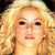 Pixelated close-up of a person with voluminous blonde hair, neutral expression, and visible facial features against a dark background.