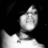 Pixelated grayscale image of a stylized figure with a rounded head and slender neck against a black background, appearing to hold or interact with a bright white shape.