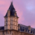 Pixelated image of a stone tower with a dark spire against a pink and purple sky background.