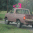 Pixelated static image of a light brown pickup truck with pink '<3' symbol above it, set against blurred green and gray background.